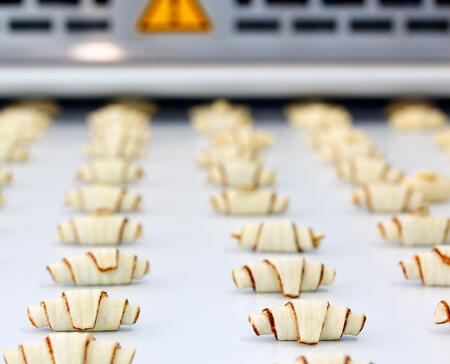 Pre-baked croissants on food processing belt conveyor